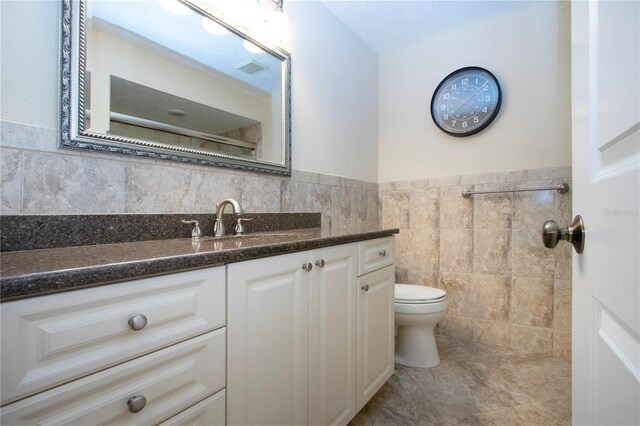 3843 El Poinier Ct W Unit 8720, Sarasota, FL 34232 - bathroom featuring toilet, vanity, tile walls, wainscoting, and tile patterned flooring