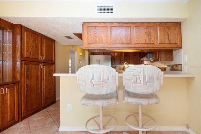 3843 El Poinier Ct W Unit 8720, Sarasota, FL 34232 - kitchen featuring freestanding refrigerator, brown cabinets, decorative backsplash, and light tile patterned floors