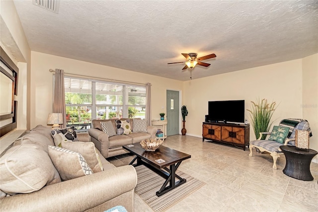 living area featuring light tile patterned floors, ceiling fan, baseboards, visible vents, and a textured ceiling