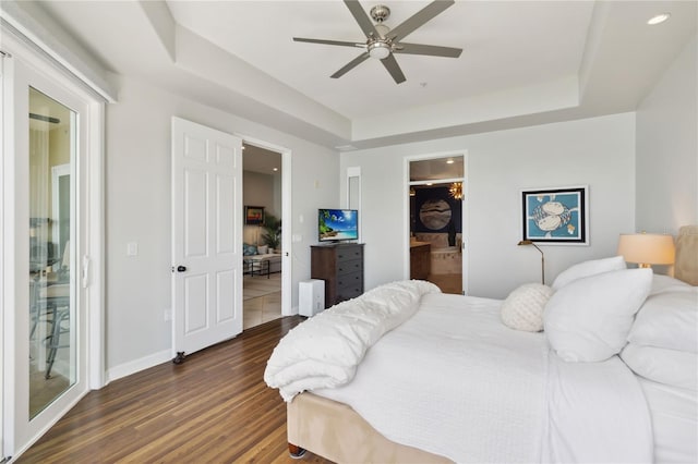 bedroom featuring recessed lighting, dark wood-type flooring, a tray ceiling, baseboards, and a spacious closet