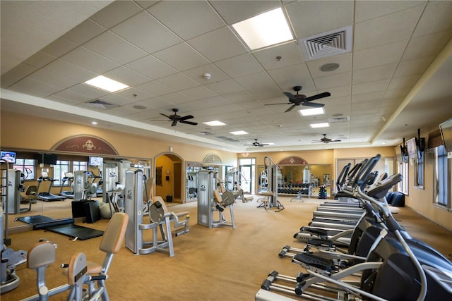 workout area featuring a ceiling fan, a drop ceiling, arched walkways, and carpet