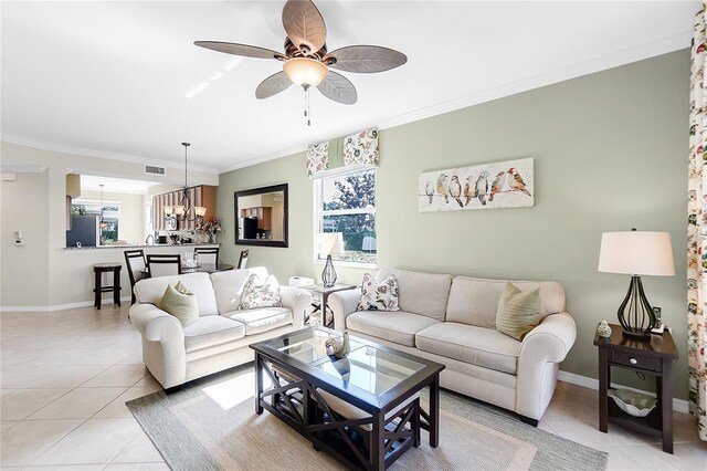 living area with light tile patterned flooring, crown molding, baseboards, a ceiling fan, and a chandelier