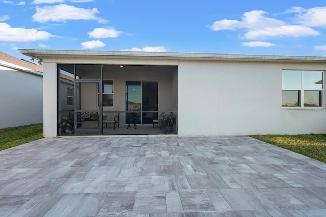 back of house featuring stucco siding, a sunroom, and a patio area
