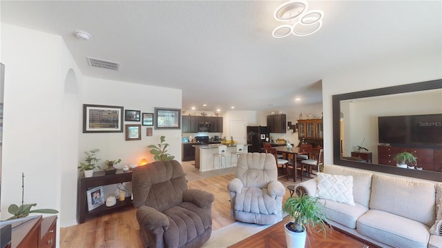 living room with arched walkways, visible vents, recessed lighting, and light wood finished floors