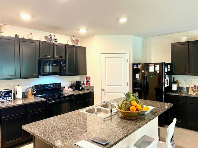 kitchen with light tile patterned flooring, a sink, an island with sink, a kitchen bar, and black appliances