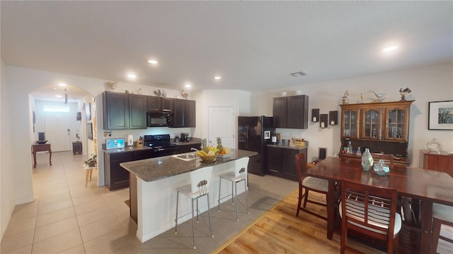 kitchen with a kitchen bar, arched walkways, a center island with sink, black appliances, and recessed lighting
