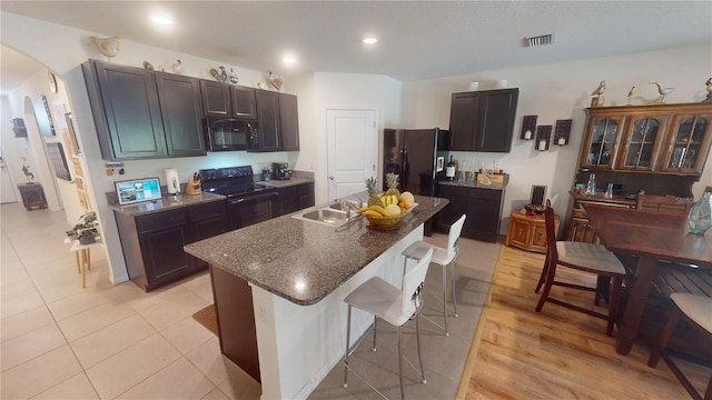 kitchen featuring a kitchen island with sink, a kitchen bar, visible vents, arched walkways, and black appliances