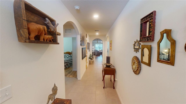 hallway featuring visible vents, arched walkways, baseboards, and light tile patterned floors