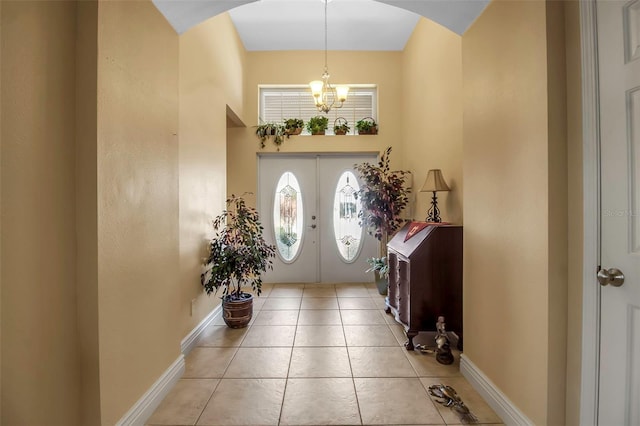 foyer with tile patterned flooring, arched walkways, an inviting chandelier, and baseboards