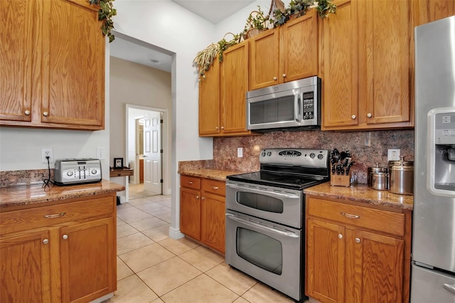 kitchen featuring light tile patterned floors, light stone counters, stainless steel appliances, and tasteful backsplash