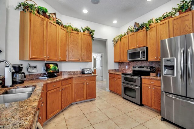 kitchen featuring light stone countertops, decorative backsplash, stainless steel appliances, a sink, and light tile patterned flooring