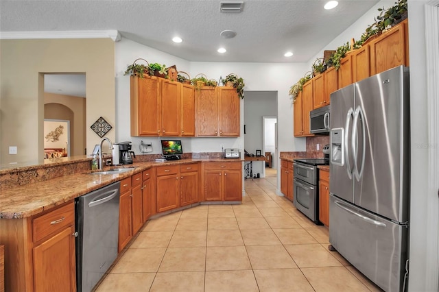 kitchen featuring light tile patterned floors, stainless steel appliances, brown cabinets, a sink, and a peninsula