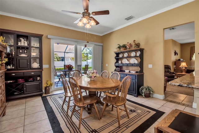 dining room featuring light tile patterned floors, ceiling fan, visible vents, baseboards, and ornamental molding