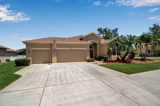 view of front facade with stucco siding, fence, a garage, driveway, and a front yard