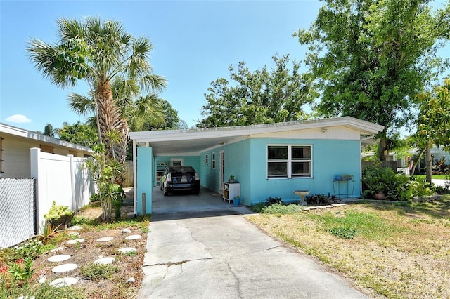 view of front facade featuring stucco siding, fence, driveway, and an attached carport