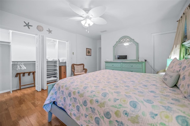 bedroom with two closets, ceiling fan, visible vents, and wood finished floors