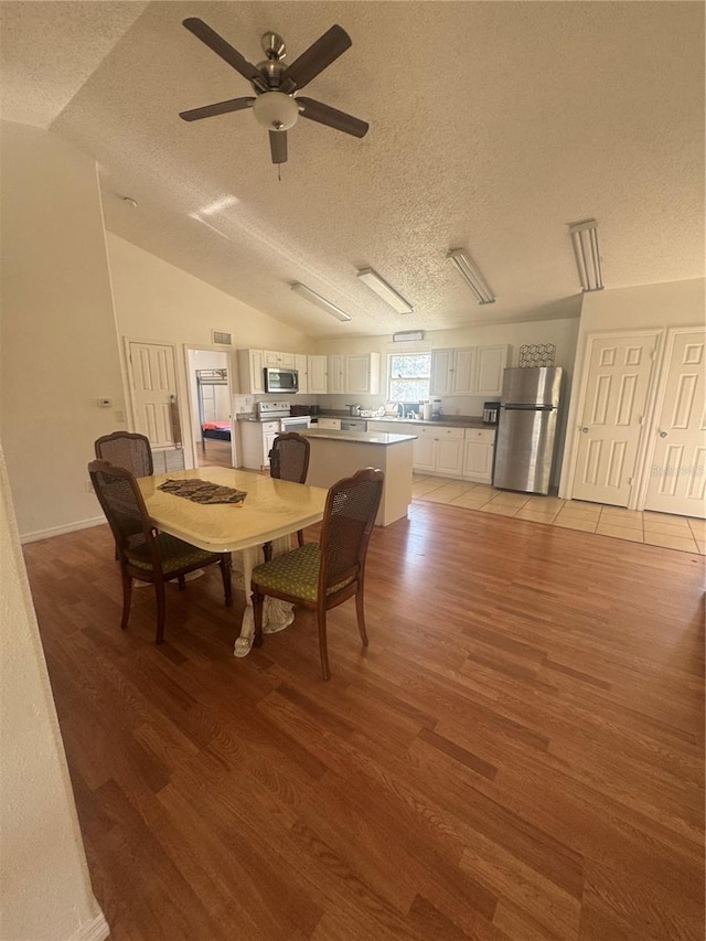 dining space featuring a textured ceiling, ceiling fan, light wood finished floors, and vaulted ceiling