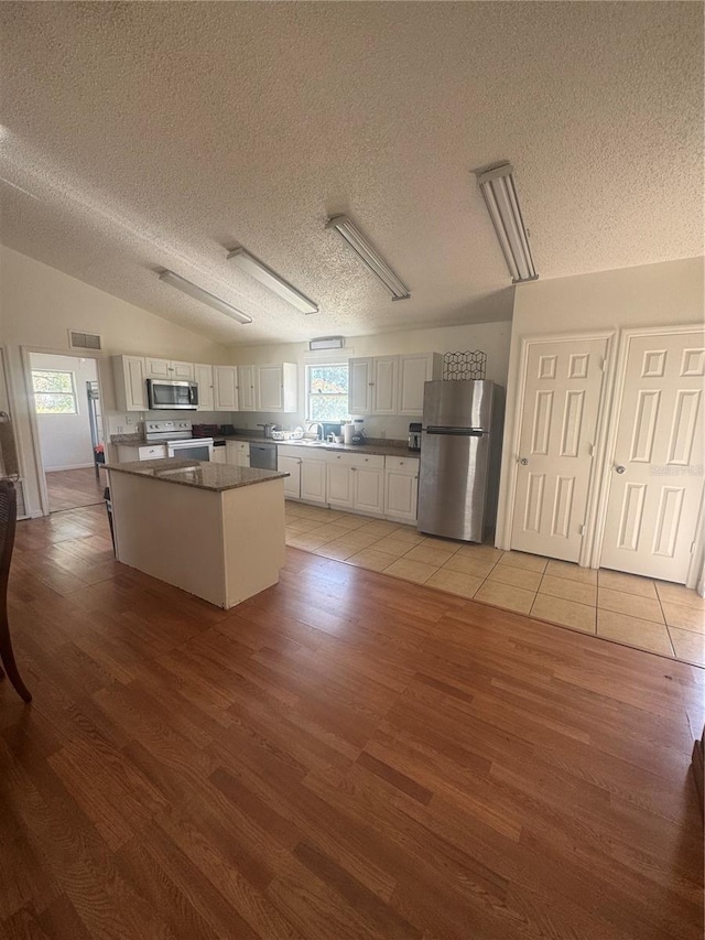 kitchen featuring stainless steel appliances, a kitchen island, light wood finished floors, visible vents, and a textured ceiling
