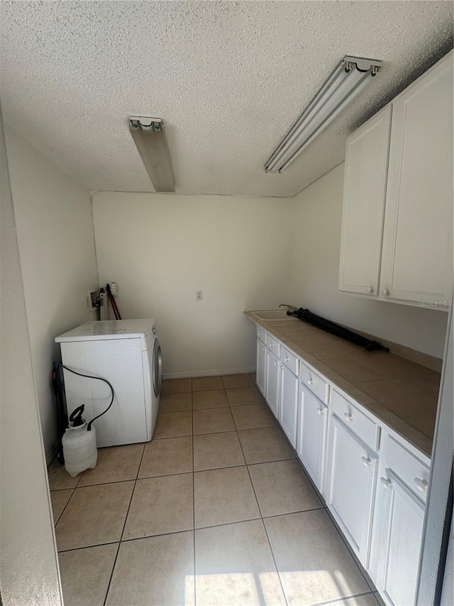 laundry room with a textured ceiling, washer / clothes dryer, cabinet space, and light tile patterned flooring