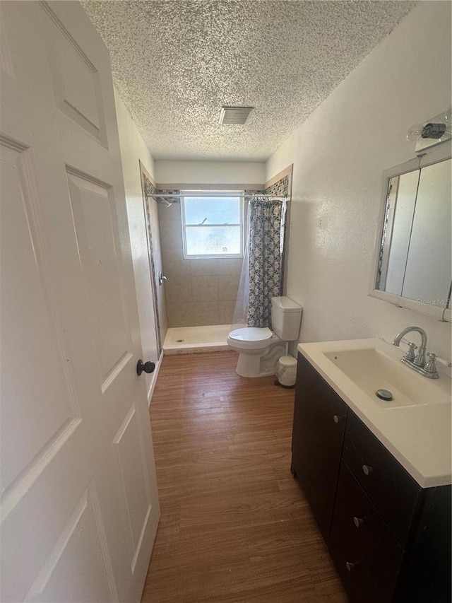 full bath with a textured ceiling, a stall shower, toilet, wood finished floors, and vanity