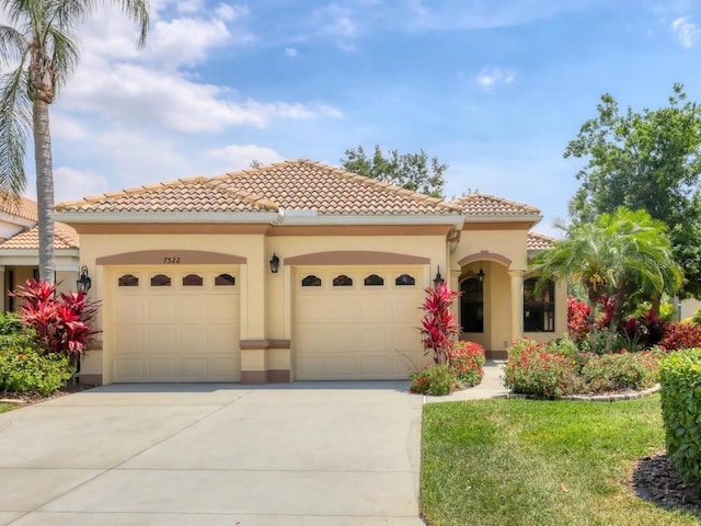 mediterranean / spanish-style house featuring stucco siding, a tile roof, a front lawn, concrete driveway, and an attached garage