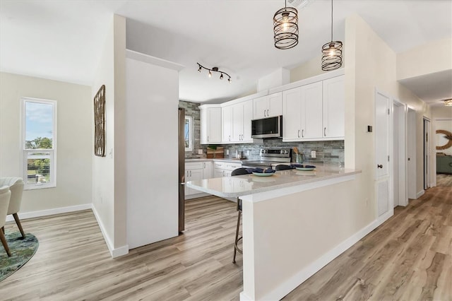 kitchen with decorative backsplash, appliances with stainless steel finishes, light countertops, white cabinets, and light wood finished floors
