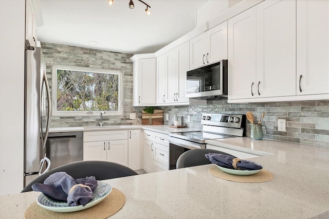 kitchen featuring stainless steel appliances, light stone counters, a sink, and tasteful backsplash