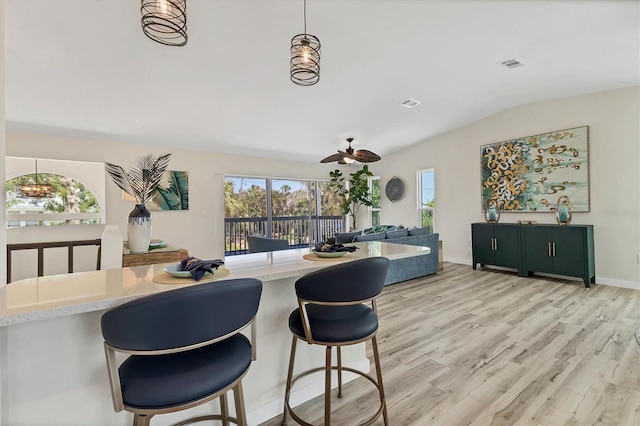 kitchen with a ceiling fan, a kitchen bar, visible vents, light stone countertops, and light wood finished floors