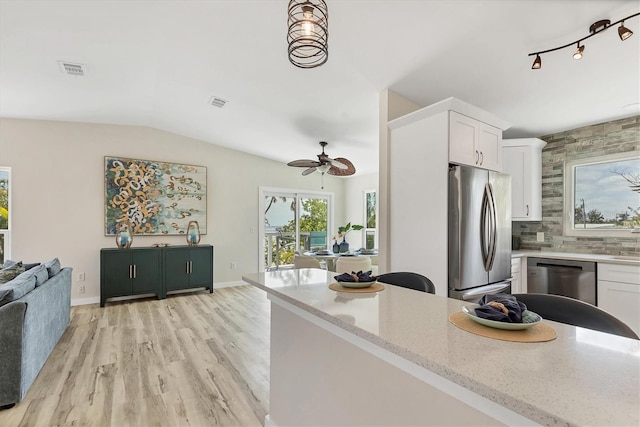 kitchen with white cabinets, ceiling fan, appliances with stainless steel finishes, light stone counters, and vaulted ceiling