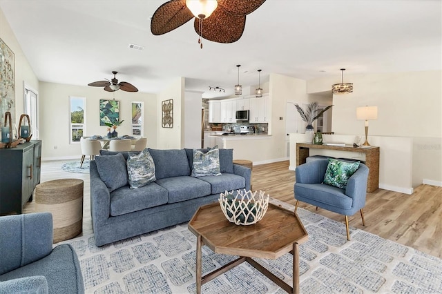 living room featuring baseboards, light wood-style flooring, ceiling fan, and visible vents
