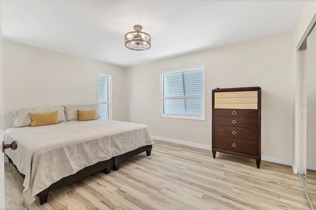 bedroom with light wood-style floors, baseboards, and an inviting chandelier