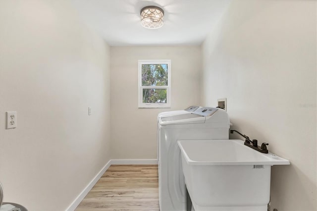 washroom with washing machine and clothes dryer, laundry area, a sink, light wood-style floors, and baseboards