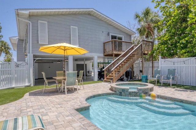 rear view of property with a deck, a pool with connected hot tub, stairway, fence, and a patio