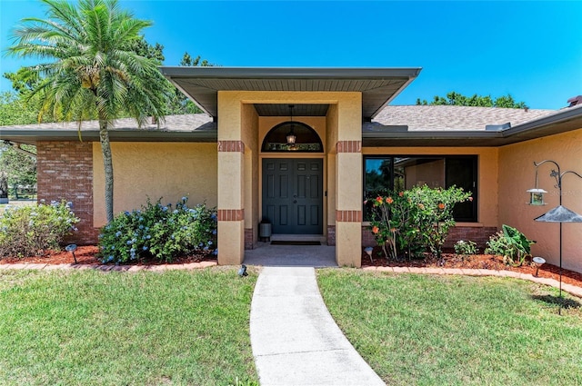 view of exterior entry with a lawn, a shingled roof, and stucco siding