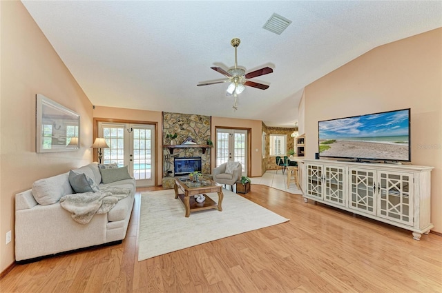 living room featuring visible vents, wood finished floors, a stone fireplace, a ceiling fan, and vaulted ceiling