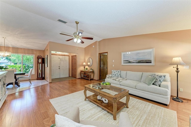 living room with light wood-style flooring, ceiling fan with notable chandelier, baseboards, vaulted ceiling, and visible vents