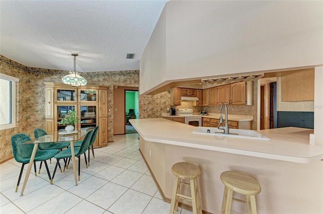 kitchen with white electric range, a sink, a peninsula, under cabinet range hood, and wallpapered walls