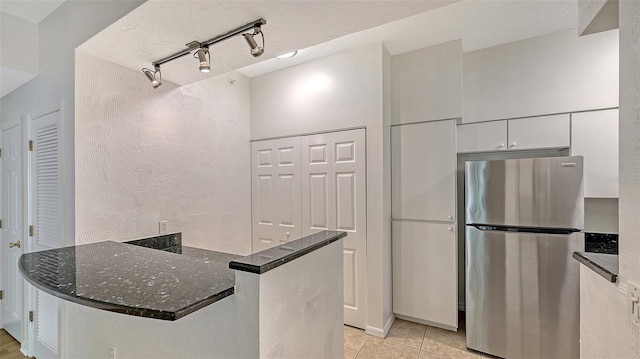 4264 Central Sarasota Pkwy Unit 111, Sarasota, FL 34238 - kitchen with freestanding refrigerator, white cabinetry, light tile patterned floors, dark stone counters, and rail lighting