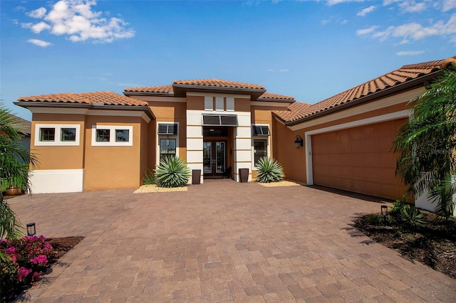mediterranean / spanish home featuring french doors, stucco siding, a garage, a tile roof, and decorative driveway