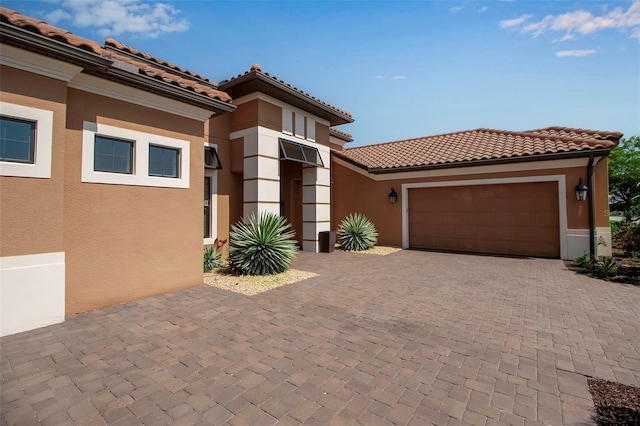 view of front of house with an attached garage, stucco siding, decorative driveway, and a tiled roof