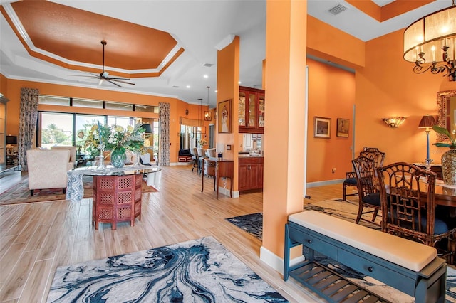 living room with a raised ceiling, ceiling fan, light wood-type flooring, baseboards, and ornamental molding