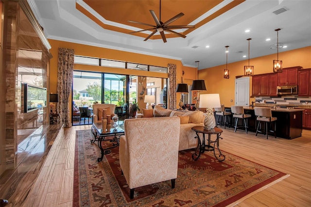 living room featuring a tray ceiling, ceiling fan, light wood finished floors, crown molding, and recessed lighting