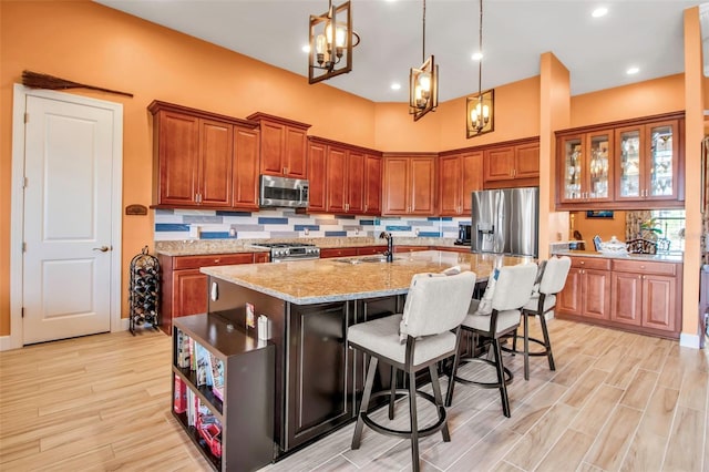 kitchen with stainless steel appliances, brown cabinetry, an island with sink, a kitchen bar, and light wood-style floors