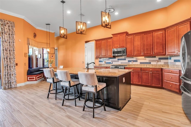 kitchen featuring stainless steel appliances, a sink, light stone countertops, a center island with sink, and hanging light fixtures