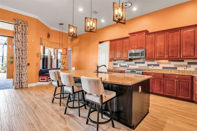 kitchen with stainless steel appliances, a chandelier, light stone counters, an island with sink, and hanging light fixtures