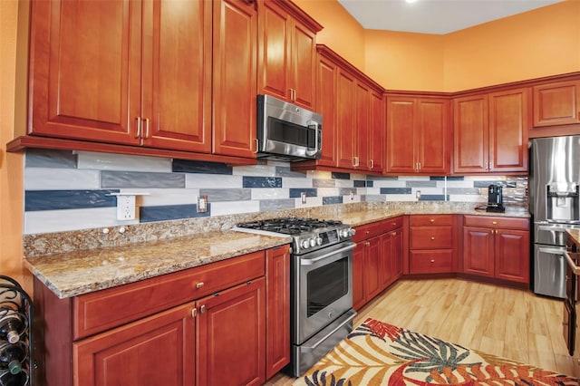 kitchen with stainless steel appliances, light stone countertops, backsplash, and light wood-style flooring
