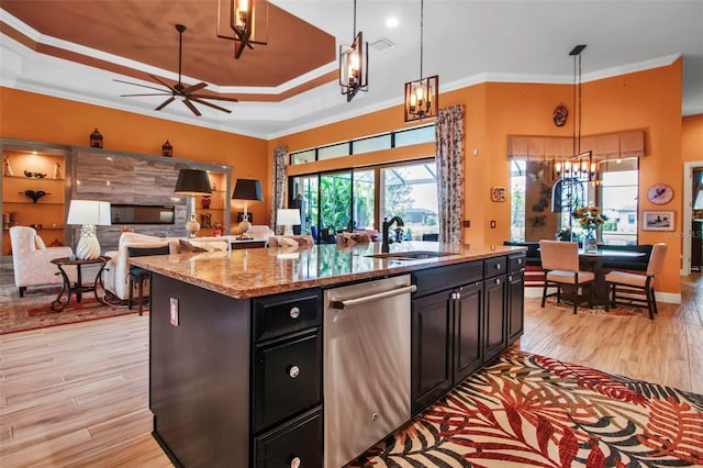 kitchen with stainless steel dishwasher, a chandelier, a tray ceiling, light wood finished floors, and ornamental molding