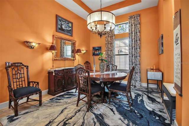 dining space with a chandelier, baseboards, a high ceiling, wood finished floors, and a raised ceiling