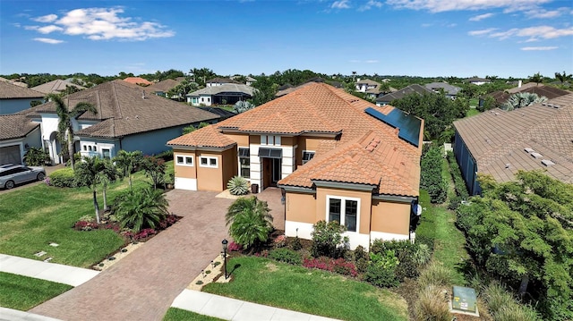 mediterranean / spanish house featuring decorative driveway, a tile roof, a residential view, an attached garage, and stucco siding
