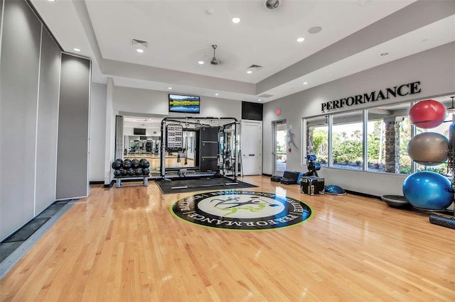 gym featuring wood finished floors, recessed lighting, and a raised ceiling